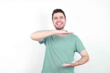 Wall Mural - young handsome caucasian man wearing green t-shirt against white background gesturing with hands showing big and large size sign, measure symbol.