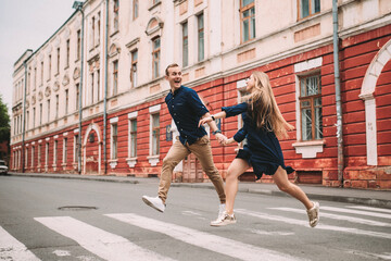 Wall Mural - A happy married couple in love runs down the street and rejoice. Beautiful young couple holding hands and smiling while walking along the city street