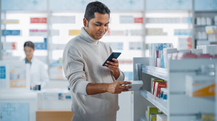 Pharmacy Drugstore: Portrait of a Handsome Young Indian Man Using Smartphone Device, Chooses to Purchase Best Medicine, Drugs, Vitamins. Shelves full of Sport Supplements, Health Care Products