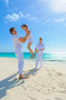 © TRAVEL EASY - Family at the beach, mother, father and daughter playing on the sand dressed in white tropical outfits