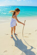Young girl at the beach, writting on the sand with wodden stick, with outfit