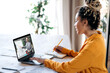 © Kateryna - E-learning by video call. African American female student learning at home using a laptop, listens to an online lesson, on laptop screen male tutor shows financial information on whiteboard,take notes