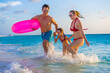 © TRAVEL EASY - Family at the beach, mother, father and daughter in the water with pink lifesaver