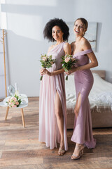 Poster - elegant interracial bridesmaids with wedding bouquets smiling at camera in bedroom.