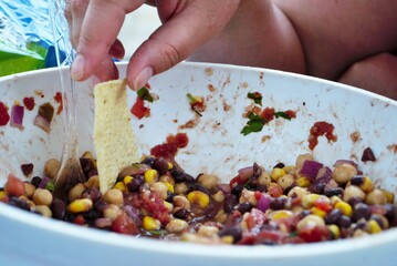 Wall Mural - hand dipping tortilla chip into fresh black bean and corn salad in a large serving bowl