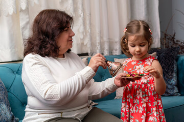 Grandmother give to her cute little granddaughter candies during Ramadan feast (aka: Ramazan or Seker bayrami). Sweets in little child girl  hands as a tradition in middle eastern culture. Real people