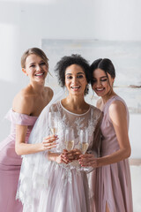 Wall Mural - joyful african american bride holding champagne near friends in bedroom.