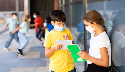 Portrait of primary school girl and boy wearing protective face masks talking outside before lesson, new normal during coronavirus pandemic situation