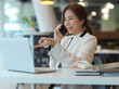 © bongkarn - Female entrepreneur in white suit talking on the phone with her partner and working with laptop