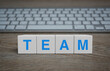 © grapestock - TEAM letter on white block cubes on wooden table with modern computer keyboard, Business teamwork communication online concept