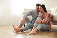 Happy Couple Sitting On Warm Floor In Living Room. Heating System