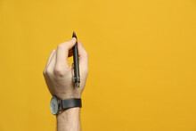 Left-handed Man Holding Pen On Yellow Background, Closeup. Space For Text