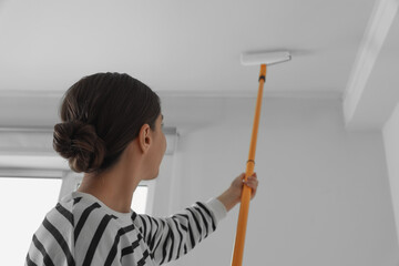 Canvas Print - Young woman painting ceiling with white dye indoors, back view