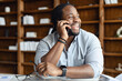 © Vadim Pastuh - Cheerful African-American male employee wearing smart casual shirt holding phone conversation, a man sitting at the desk in modern office, a biracial entrepreneur talking over smartphone and laughs