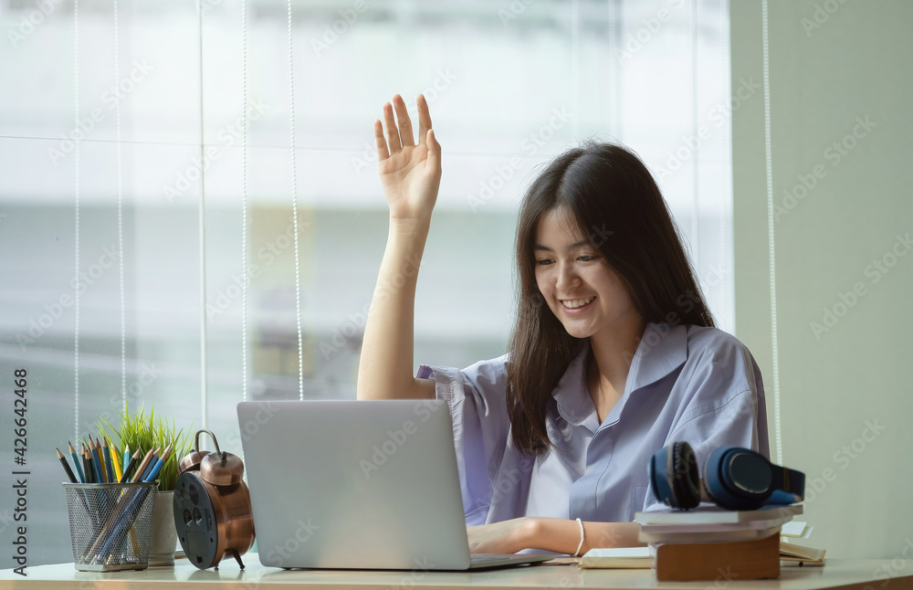 Online education. The girl raises her hand to answer the teacher's question at home - obrazy, fototapety, plakaty 