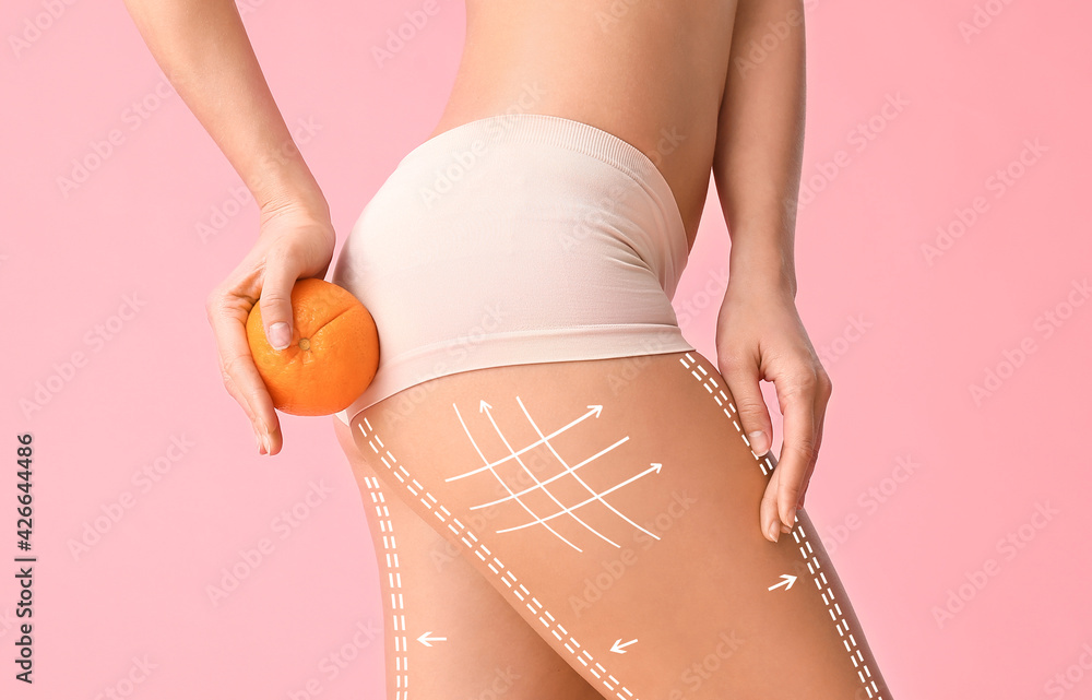 Young woman with orange fruit on color background. Concept of cellulite - obrazy, fototapety, plakaty 