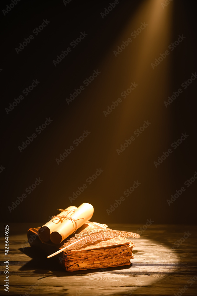 Old book with scrolls and feather against dark background - obrazy, fototapety, plakaty 
