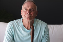 Caucasian Senior Man In Living Room Sitting On Couch In Thought Holding Walking Stick