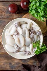 Wall Mural - Raw cuttlefish in a ceramic plate on the kitchen table. Lots of peeled squid in a bowl on a brown wooden table top view. The concept of cooking shellfish