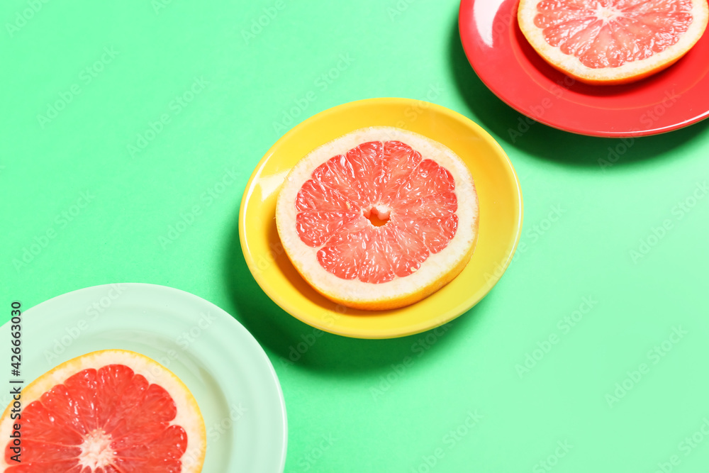Plates with slices of ripe grapefruit on color background