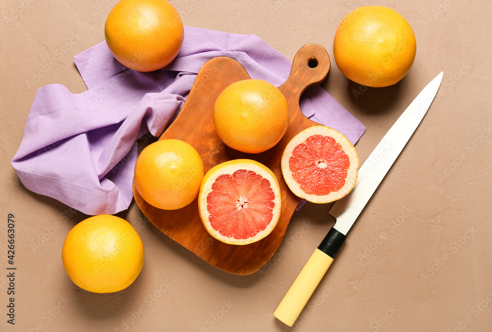 Board with ripe grapefruits and knife on color background