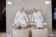 © zinkevych - Senior couple in white robes having procedures for legs in spa salon