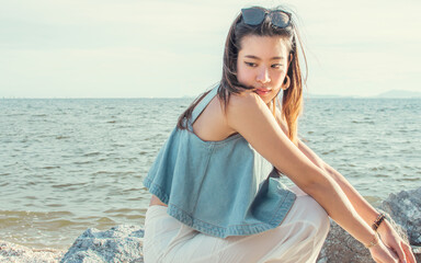 Asian beautiful woman wearing casual shirt and sitting on the beach beside sea in sunny day.