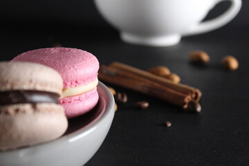 Wall Mural - Macaroons on a gray plate at the back stands a cup of coffee or tea coffee beans and cinnamon sticks on a black background with a place for text and with a copyspace