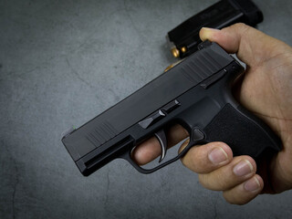 Man's hand holds a black 9 mm. cylinder gun on a black cement background.