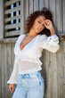 © czamfir - A beautiful woman with curly hair poses near an old wooden house. fashion style.