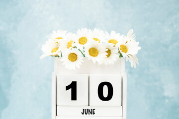 cube calendar for June with daisy flowers over blue with copy space