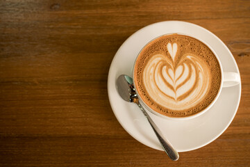 Hot coffee latte with latte art milk foam in cup mug on wood desk on top view. As breakfast In a coffee shop at the cafe,during business work concept