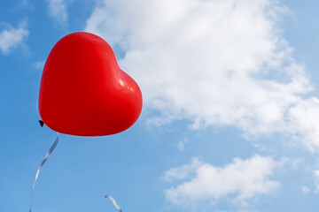 red heart-shaped balloon on blue sky background with clouds