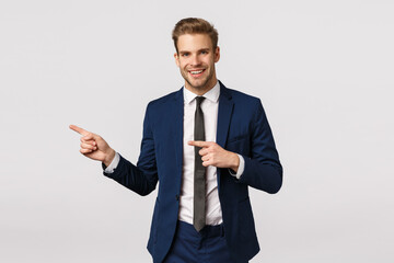Stylish and confident, handsome blond bearded man in classic blue suit, pointing left, showing business partner place where discuss meeting, invite come inside office, standing white background
