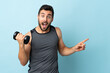 © luismolinero - Young sport man with beard making weightlifting surprised and pointing finger to the side