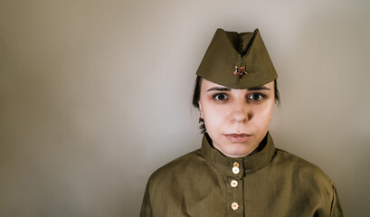 Portrait of young woman in uniform on background of gray wall. Female in Soviet military uniform while of the Second World War.