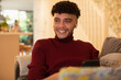 © Sam Edwards/Caia Image - Happy young man listening to music with earbuds on sofa