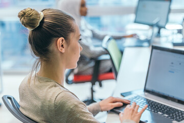 Blonde businesswoman working on her pc while sitting in a crowded modern office.