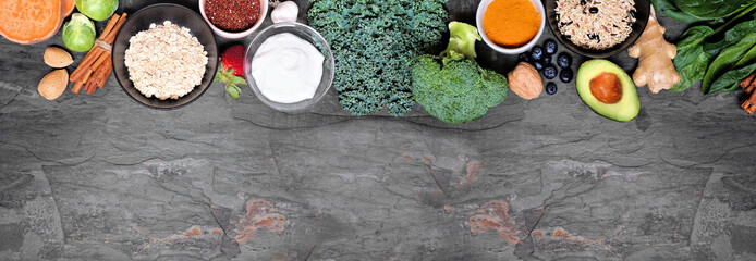 Wall Mural - Set of healthy food ingredients. Above view top border on a slate banner background. Copy space. Super food concept with green vegetables, berries, whole grains, seeds, spices and nutritious items.