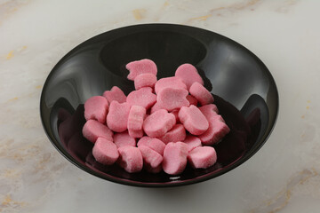 Wall Mural - Pink raspberry gummy candy pieces in black bowl on table