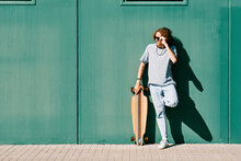 Young Man With Sunglasses And Longboard Or Skate In A Green Wall On A Summer Day
