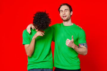 two friends in green t-shirts hugs fun red background