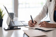 © amnaj - Close-up of a businesswoman hand holding a pen taking notes with tablet and smartphone at the office.