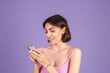 © Анастасия Каргаполов - Young brunette in top isolated on purple background holding mobile phone with big smile happy excited face, chatting, having conversation