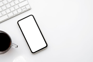 white office desk table with smartphone with blank mockup screen, cup of coffee and computer keyboar