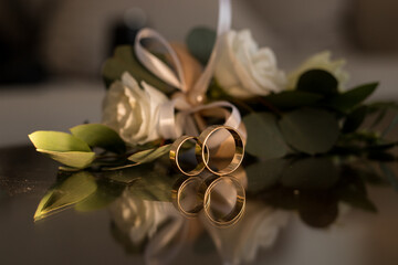 Two wedding gold rings on mirror table with bouquet of white roses