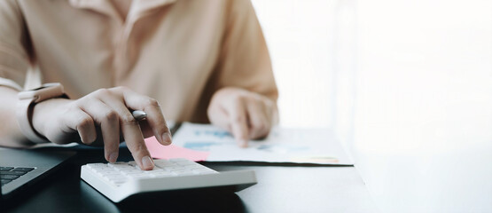 Close up Business woman using calculator and laptop for do math finance on wooden desk in office and business working background, tax, accounting, statistics and analytic research concept