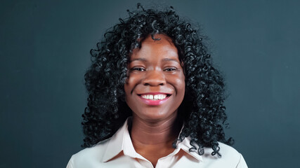 Positive young African-American woman with curly hair turns head and smiles looking into camera on black background in studio close view