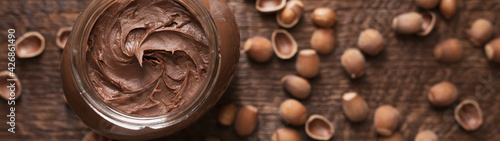 Obraz Dibond Chocolate-nut paste spread in a glass jar on a wooden background banner