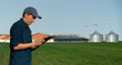 © scharfsinn86 - Farmer with tablet computer on a background of modern dairy farm using renewable energy, solar panels and wind turbines